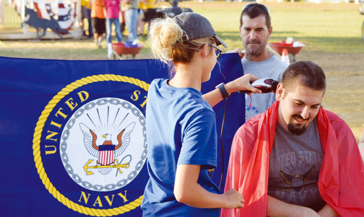 Kelsey Friend, left, was one of the audience members who had her name drawn to help shave the head of Navy-bound George Hesler in a ceremony held on Saturday night of the Adams County Fair.