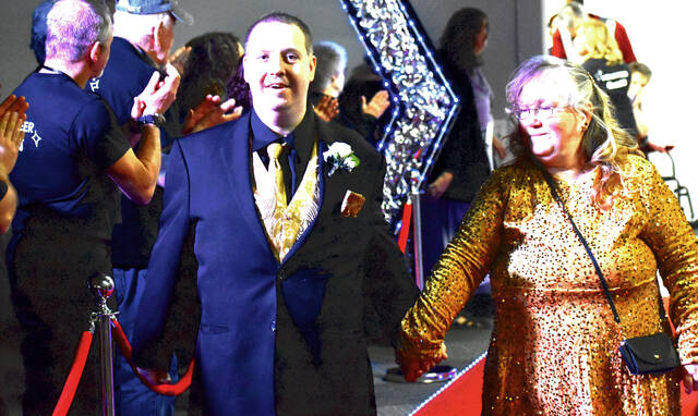 A Night to Shine honored guest walks the red carpet with a friend as cheering volunteers line the walkway, creating the signature grand entrance that welcomes more than 120 guests each year. (Photo by Ryan Applegate)